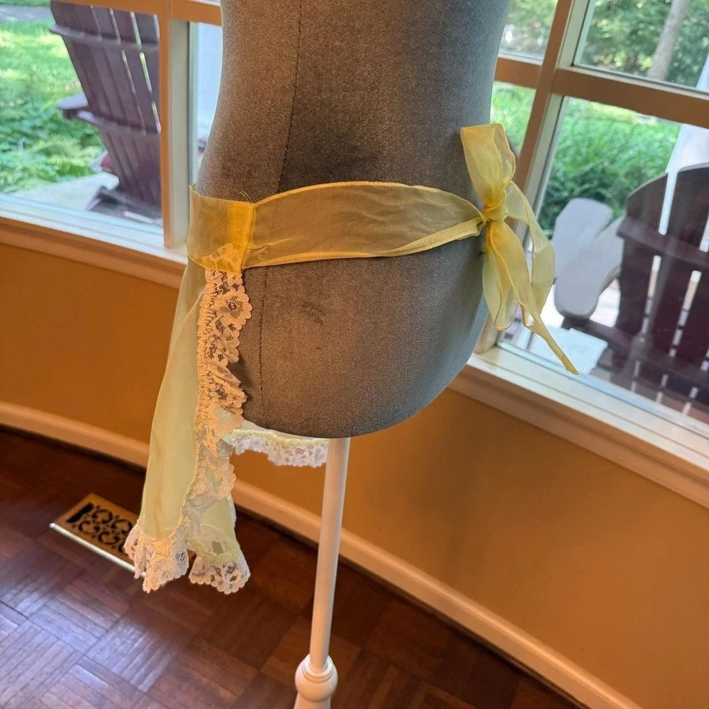 Vintage sheer yellow apron with ornate white lace trim and a bow-accented pocket